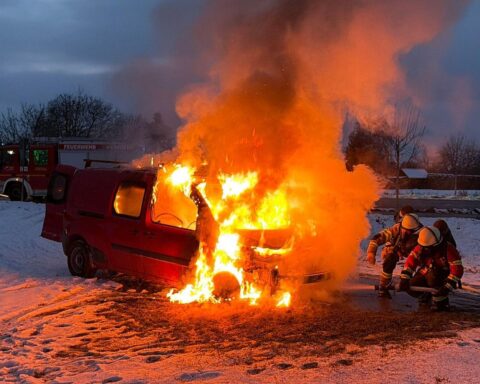 Feuerwehr löscht brennendes Auto auf Feld in Weinheim; Einsatzkräfte arbeiten unter Atemschutz.