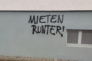 Graffiti mit Schriftzug "Mieten runter", symbolisiert Protest gegen hohe Mieten und Mietmarktprobleme.