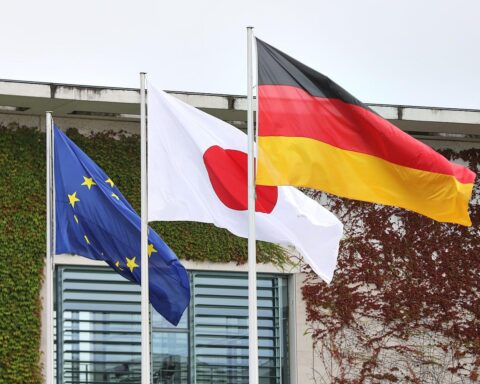 Fahnen von Deutschland, Japan und der EU symbolisieren Kooperation in erneuerbaren Energien und Medizintechnik.