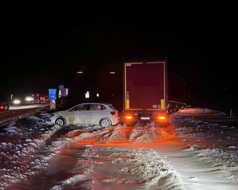 Verkehrsunfall mit drei Fahrzeugen auf schneebedeckter Autobahn, Polizei am Einsatzort.