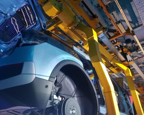 Bild zeigt moderne Automobilproduktion mit Maschinen und Arbeitern, symbolisiert Industrie-Wachstum und Innovation.