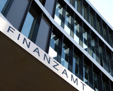 Ein überfülltes Finanzamt mit gestressten Mitarbeitern und veralteter Büroausstattung.