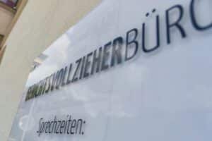 Gerichtsvollzieher im Einsatz, umgeben von nötiger, jedoch fehlender Schutzausrüstung und Arbeitsgeräten.