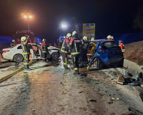 Unfallstelle mit zwei beschädigten Autos, Feuerwehr im Einsatz, Rettungsaktion für eingeklemmten Fahrer.