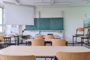 Leerer Klassenraum, Schreibtische und Stühle, Symbol für abgesagten Präsenzunterricht wegen Wetterbedingungen.