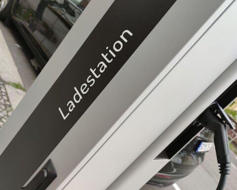 E-Auto an Ladestation, umgeben von technologischen Symbolen und Sicherheitswarnungen.