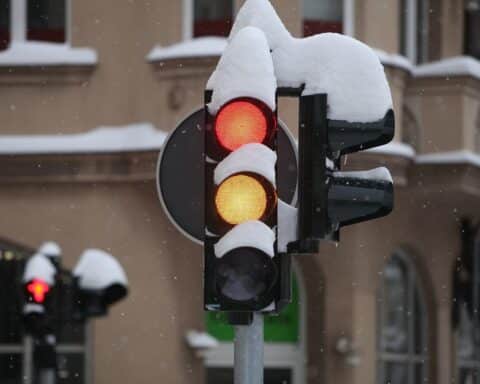 Verschneite Ampel mit schneebedecktem Straßenbelag und bedecktem Himmel, winterliche Stimmung.