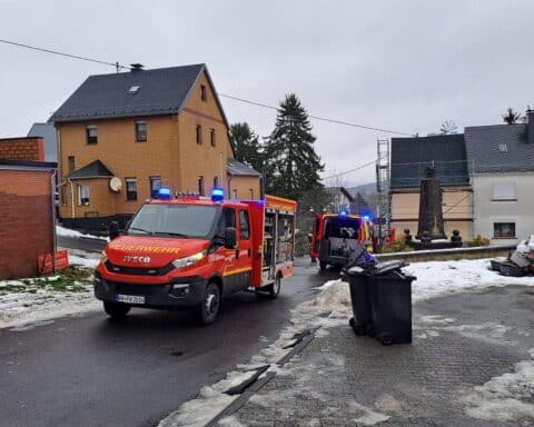 Feuerwehrleute löschen einen Zimmerbrand in einem Wohnhaus, starke Rauchentwicklung sichtbar.