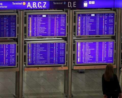 Frau vor Informationstafel am Flughafen, zeigt Verspätungen und Flugausfälle wegen Winterwetter an.