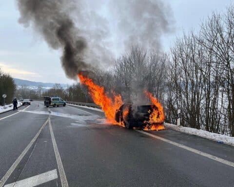 Ein brennendes Auto auf einer Landstraße, Feuerwehrleute löschen das Feuer.