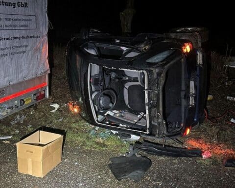 Verunfallter Smart auf der Seite, beschädigtes Glasdach, winterliche Straßenverhältnisse, Polizei vor Ort.