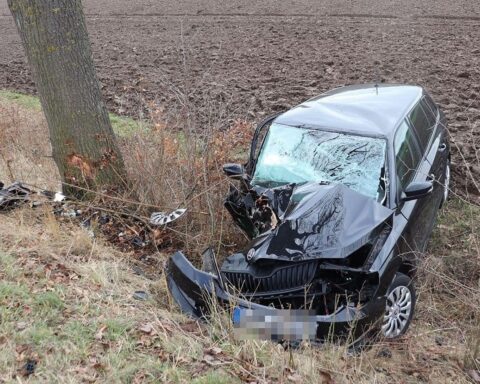 Verunfallter schwarzer PKW, schwer beschädigt, im Straßengraben neben einem Baum.