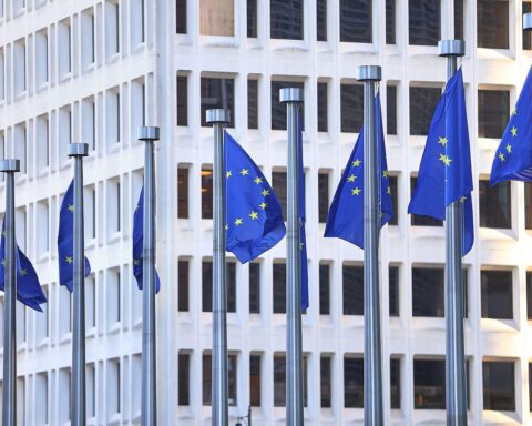 EU-Fahnen vor europäischem Parlament; Symbol für Handelsabkommen und internationale Zusammenarbeit.