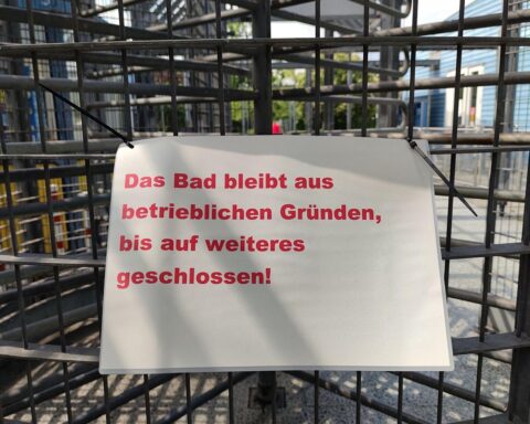 Ein leerer Schwimmbeckenbereich, umgeben von verlassenen Liegen und Schildern über Schließungen.