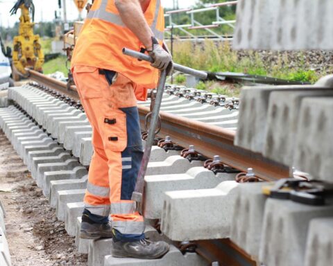 Bauarbeiten an Gleisen mit Baustellenfahrzeugen, Arbeitern und Absperrungen im Hintergrund.