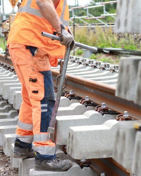 Bauarbeiten an Gleisen mit Baustellenfahrzeugen, Arbeitern und Absperrungen im Hintergrund.