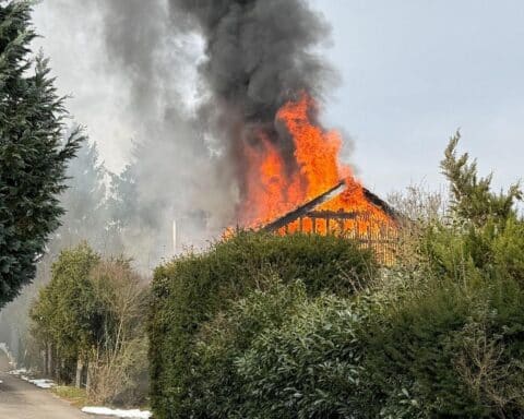 Rauch und Flammen über einem Wohnhaus, Feuerwehr im Einsatz zur Brandbekämpfung.