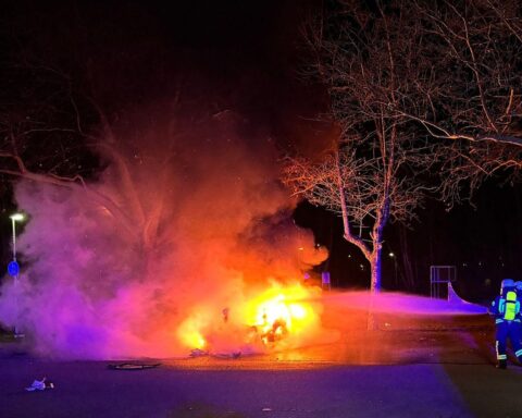 Ein brennender Tesla auf einem leeren Parkplatz, mit Feuerwehr im Einsatz.