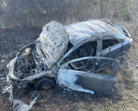 Ausgebranntes Fahrzeug im Straßengraben nach Unfall, Polizei und Feuerwehr am Unfallort.