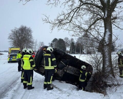 Rettungskräfte befreien Fahrer aus Unfallwagen, der im Graben liegt, auf glatter Straße.