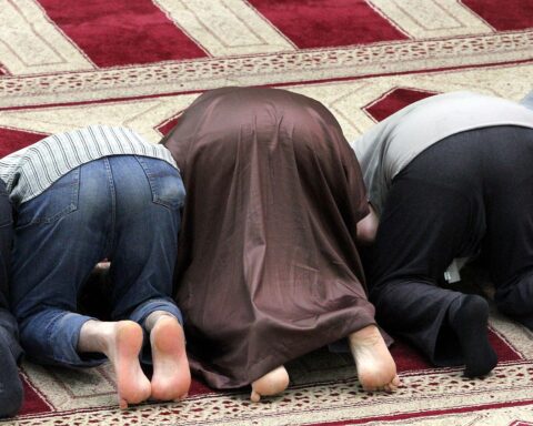 Gläubige Muslime beten in einer Moschee, symmetrisches Bild, feierliche Atmosphäre, Gemeinschaft.