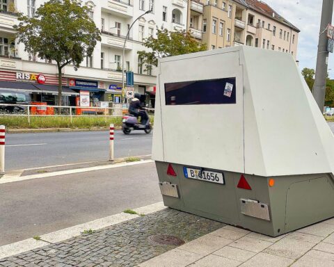 Mobiler Blitzer an einer Straße, umgeben von Verkehrsschildern und Fahrzeugen, symbolisiert Verkehrssicherheit.