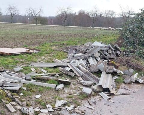 Illegal abgelagerter Bauschutt auf einem Feldweg, umgeben von Natur und angrenzenden Straßen.