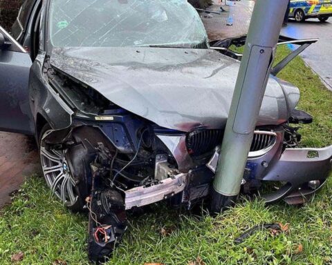 Verunfallter grauer BMW, Polizei vor Ort, beschädigte Straßenlaternen und Verkehrsschild sichtbar.