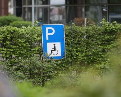 Behindertenparkplatz mit Symbolen für Barrierefreiheit und Reformforderungen zur Inklusion.