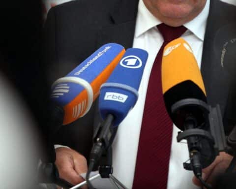 Mikrofone vor einem öffentlich-rechtlichen Logo, symbolisierende Rundfunkbeitragserhöhung und Medienvielfalt.