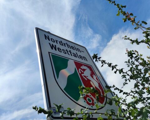 Nordrhein-westfälisches Landesschild vor Industrie- und Handelskulisse, symbolisiert Wirtschaft und Exporte.