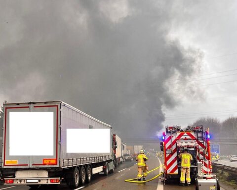Brennender Lastwagen auf Autobahn, Feuerwehr im Einsatz, Rauch und Verkehrsbehinderungen sichtbar.