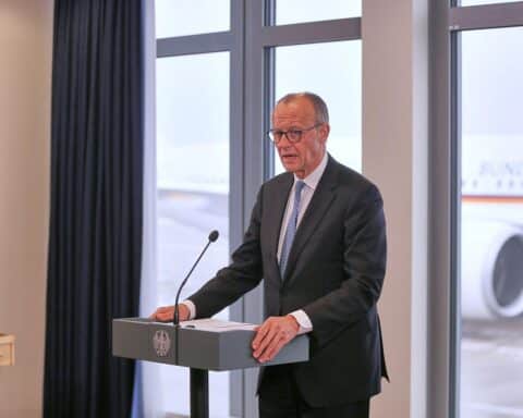 Friedrich Merz bei offizieller Reise, im Hintergrund Gespräche über Frieden zwischen Ukraine und Russland.