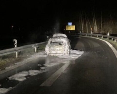 Flammen schlagen aus einem brennenden PKW an der Autobahn, Feuerwehr im Löscheinsatz.