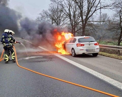Feuerwehr im Einsatz an Autobahn, brennender Pkw, Rauch, Stau, Einsatzkräfte mit Equipment.