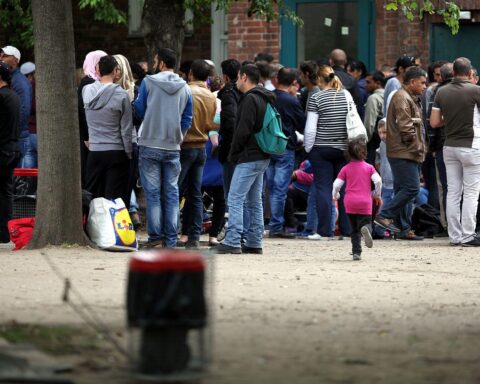 Flüchtlinge warten an einer Aufnahmestelle, symbolisiert Integration und Arbeitsmöglichkeiten in Deutschland.