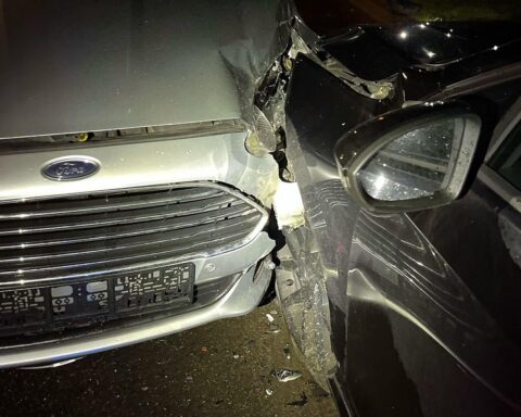 Unfallstelle mit beschädigten Fahrzeugen und Polizeiautos, Behandlung einer verletzten älteren Frau.