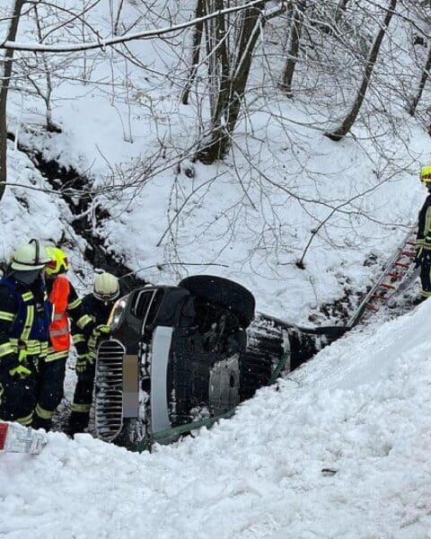 Rettungskräfte bergen Verletzte nach schwerem Unfall auf winterglatter Straße, BMW im Bachbett.