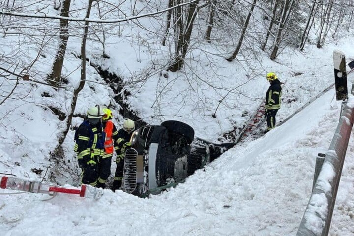 Rettungskräfte bergen Verletzte nach schwerem Unfall auf winterglatter Straße, BMW im Bachbett.