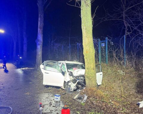 Unfallstelle mit deformiertem Auto, Feuerwehr und Rettungsdienst im Einsatz, nächtliche Umgebung.