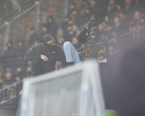 Aggressive, vermummte Fußballfans werfen Gegenstände auf Polizei während Ausschreitungen im Stadion.