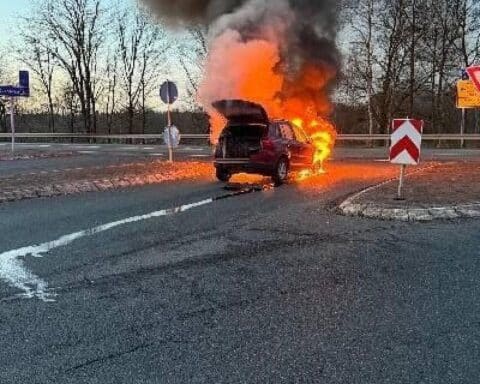 Ein brennendes Auto auf der Autobahn mit Feuerwehr und Polizei im Einsatz.