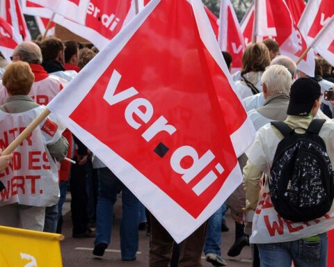 Gewerkschaftsmitglieder versammeln sich vor Hafen, Protestplakate, Warnstreik-Banner, symbolisieren Tarifverhandlungen.