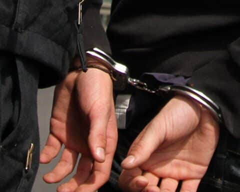 Festnahme eines mutmaßlichen Spions mit Handschellen, umgeben von Polizeibeamten.