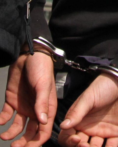Festnahme eines mutmaßlichen Spions mit Handschellen, umgeben von Polizeibeamten.