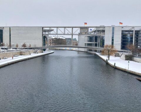 Blick auf die Spree zwischen beiden Gebäuden, symbolisiert Verzögerungen im Bundestagsbauprojekt.
