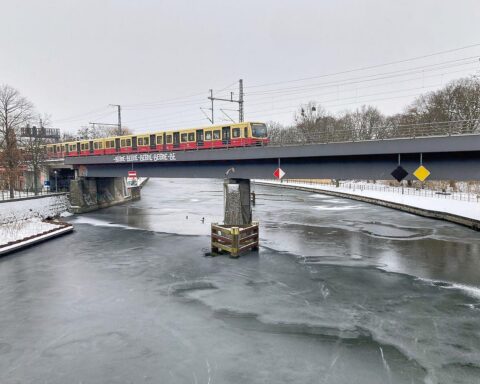 Schneebedeckte Berliner Straße, graue Wolken, glatte Straßen, winterliche Atmosphäre, frostige Temperaturen.