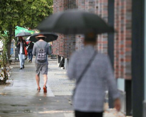 Passanten mit Regenschirmen unter einem bewölkten Himmel, während Regen und Schnee fallen.