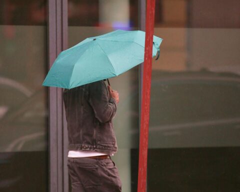 Mann mit Regenschirm unter grauem Himmel, Regen- und Schneeschauer in Nordrhein-Westfalen erwartet.