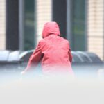 Mann mit Kapuze unter wechselhaftem Wetter, Wolken und vereinzelte Sonnenstrahlen.